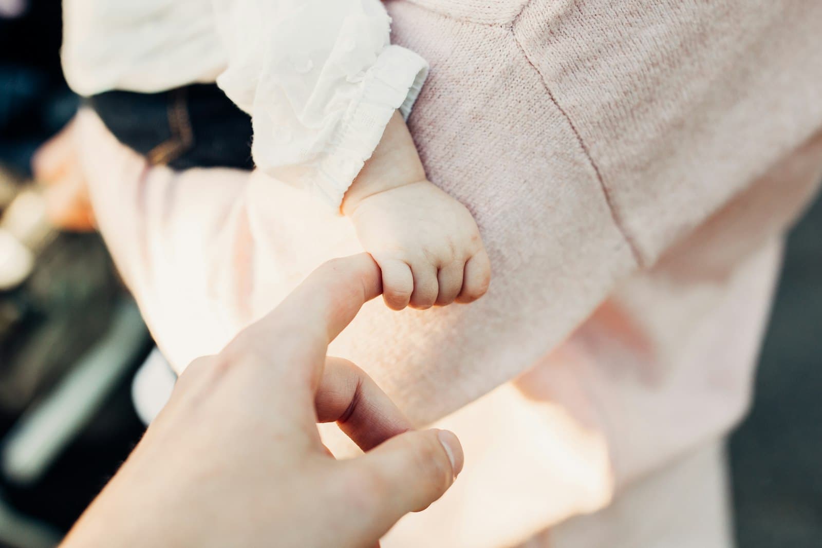 Die Hand eines Babys umgreift den Finger einer erwachsenen Person